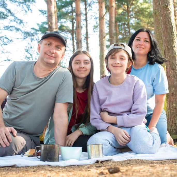 family with two children sitting on a blanket in the forest, in a tent camp on summer holidays happy stepfamily camping near therapy for blended families in Reno, NV